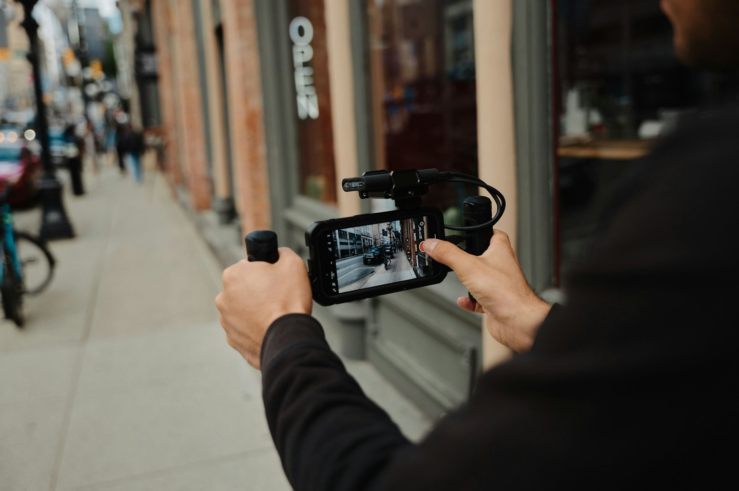 Person uses a smartphone and gimbal to record on a sidewalk.