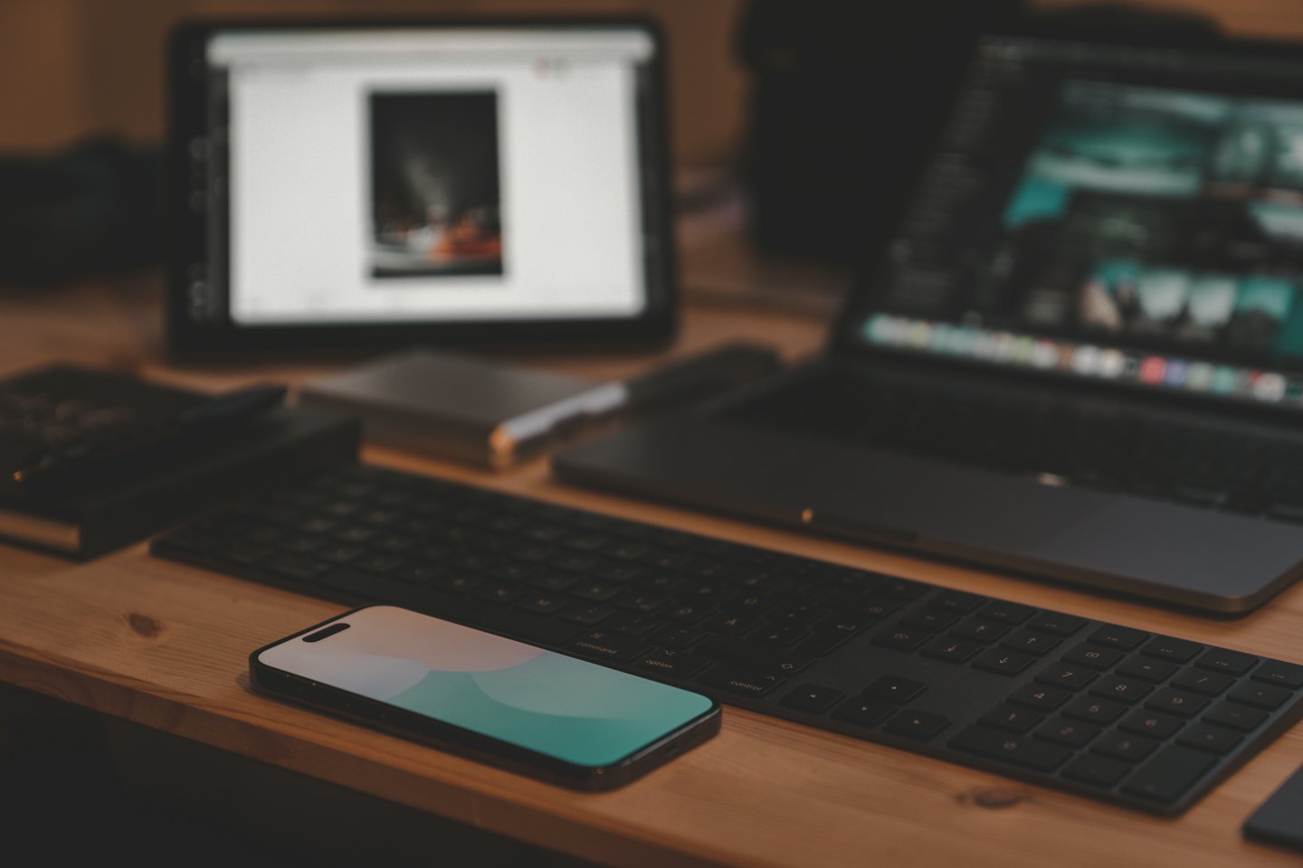 Laptop, smartphone, and keyboard arranged on a wooden desk.