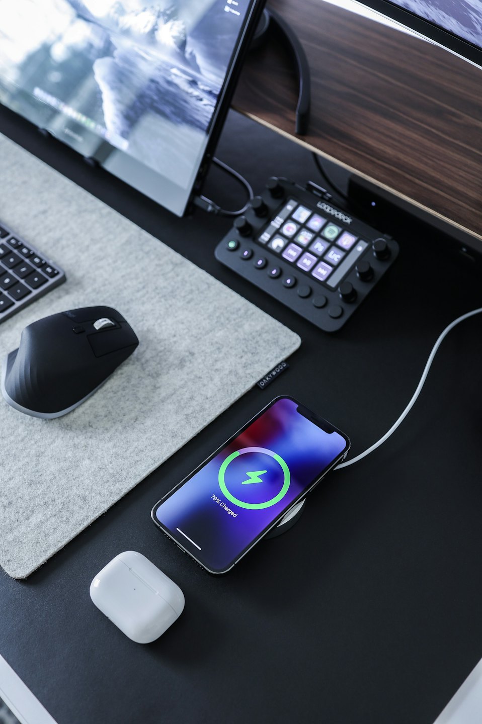 Modern desk with smartphone charging next to AirPods and keyboard.